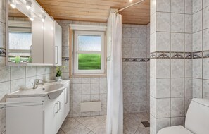 Ein Badezimmer mit Dusche, Waschbecken und einem Fenster mit Blick auf ein grünes Feld.