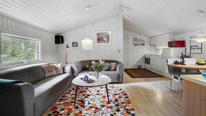 Ett modernt vardagsrum med en grå soffa, ett vitt soffbord och en färgglad matta. I bakgrunden syns ett köksområde med vita skåp och en röd mikrovågsugn.