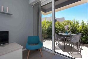 A modern room with a TV, a blue chair, and a sliding glass door leading to an outdoor patio with a table and chairs.