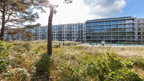 A modern apartment building with multiple balconies, a swimming pool, and a grassy area with trees.