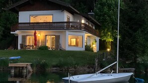 Une maison à deux étages avec un balcon, un quai avec un bateau et un étang.