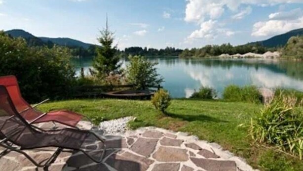 Une vue sur le lac, avec une terrasse en pierre et un fauteuil de jardin rouge.