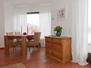 Zona pranzo con tavolo e sedie in legno, un pensile e una finestra con tende.