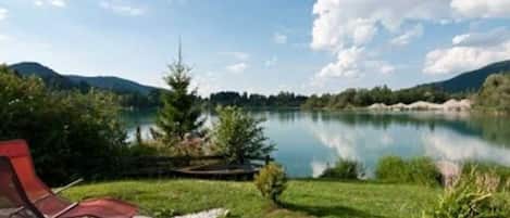 A lakeside view with a stone patio and a red lounge chair.