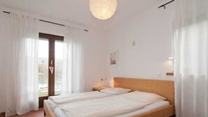 Une chambre avec un grand lit, des rideaux blancs, un luminaire suspendu et une petite table de chevet.