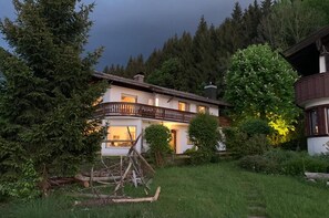 Una casa a due piani con un balcone, circondata da alberi e un prato.