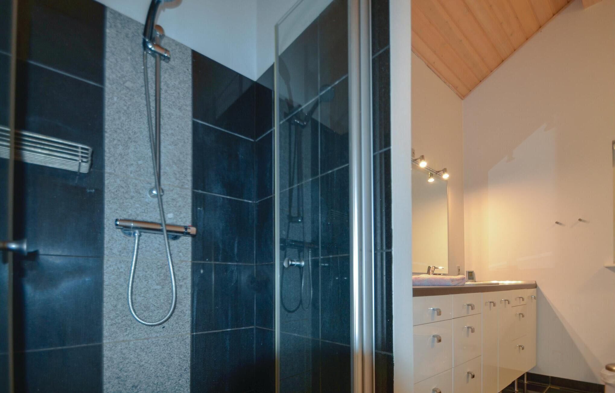 A modern bathroom with a glass shower enclosure, dark tiles, and a wooden ceiling.