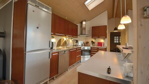 Een moderne keuken met houten kasten, roestvrijstalen apparatuur en hangende lampen.