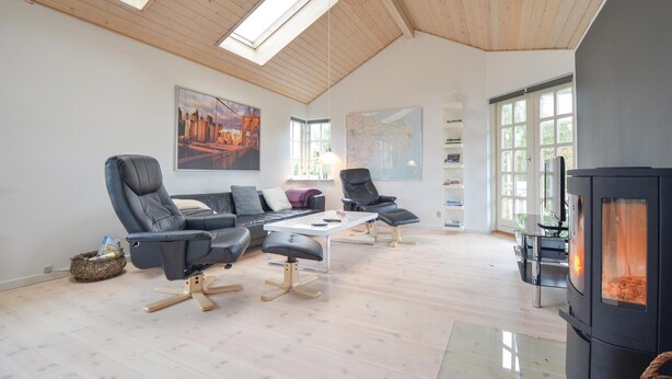 Een moderne woonkamer met een hoge plafond, houten balken, een open haard en twee zwarte leren banken.