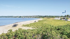 Een strand met een bankje, een vlag en een rij huizen op de achtergrond.