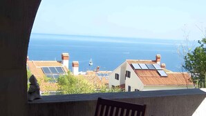 Un balcón con una mesa para dos, con vista al mar y casas a la orilla.