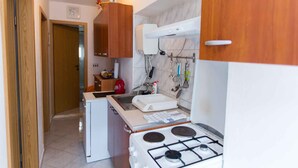 Eine kompakte Küche mit Gaskochfeld, weißen Schränken, einem kleinen Kühlschrank und einer Mikrowelle.