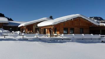 Une cabane en bois dotée d’un porche couvert et d’un toit enneigé, entourée d’un paysage hivernal.
