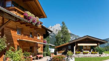A wooden chalet with balconies, a patio area, and a mountain backdrop.
