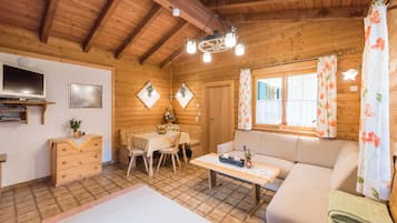 Interior de una cabaña de madera con sofá, mesa de comedor, televisor y paredes de madera.