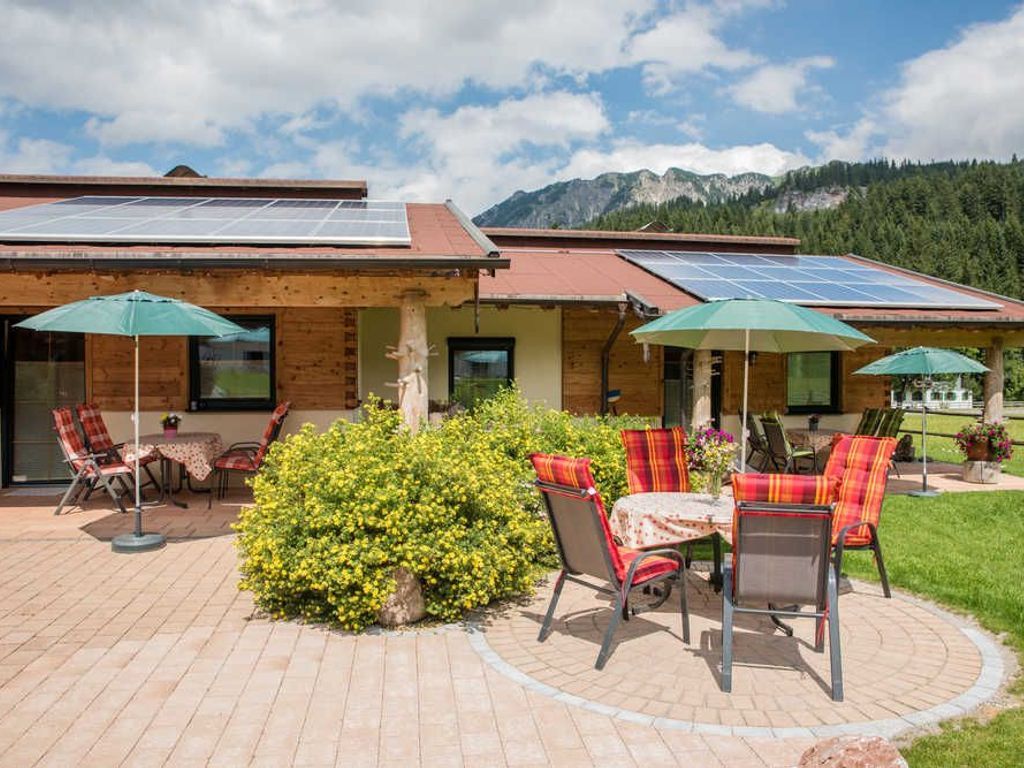 A building with solar panels on the roof, outdoor seating with chairs and tables, and a well-maintained garden area.