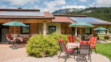 A building with solar panels on the roof, outdoor seating with chairs and tables, and a well-maintained garden area.