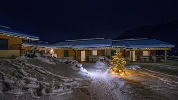 Een besneeuwde buitenruimte met een kerstboom en een gebouw met meerdere kamers en een overdekt terras.