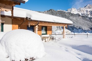 Eine Holzhütte mit schneebedecktem Dach und einer Terrasse mit Sitzgelegenheiten.