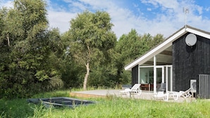 Une maison moderne dotée d’une grande porte vitrée donnant sur un espace extérieur couvert, aménagé avec des chaises blanches et une table.