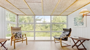 Une véranda avec de grandes fenêtres, deux chaises en bois, une petite table et une lampe.