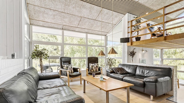 Un salon spacieux, doté de canapés en cuir, d’une table basse en bois et de grandes fenêtres donnant sur un paysage verdoyant.