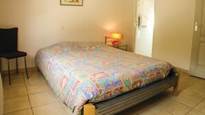 Un dormitorio con cama, una silla, una mesita de noche con lámpara y una puerta.