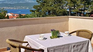 Une table recouverte d’une nappe blanche, deux chaises en osier, un petit vase avec des plantes vertes et une tasse posée sur la table.