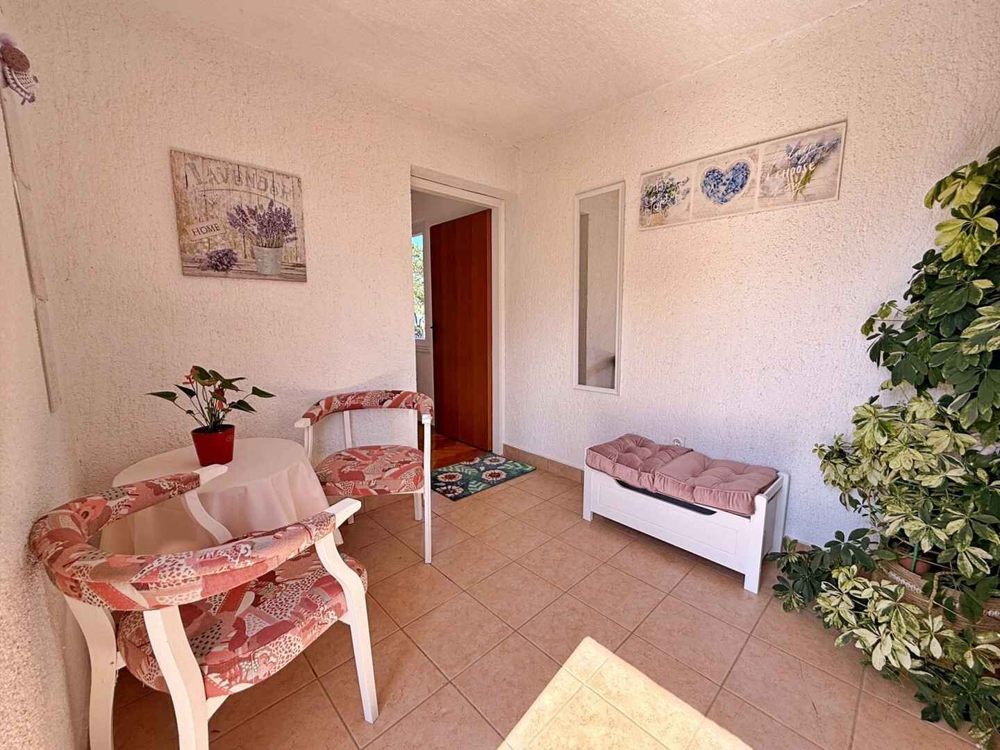 Ein kleiner, gemütlicher Raum mit einem runden Tisch, zwei Stühlen, einer Bank und einem Blumentopf.