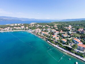 An aerial view of a coastal town with houses along the shoreline, a clear blue sea, and mountains in the background. - Holiday apartment with air conditioning and sea view (Šilo)