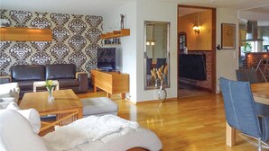 Un salon moderne avec une cheminée, un plancher en bois et un coin repas agrémenté d’une chaise bleue.