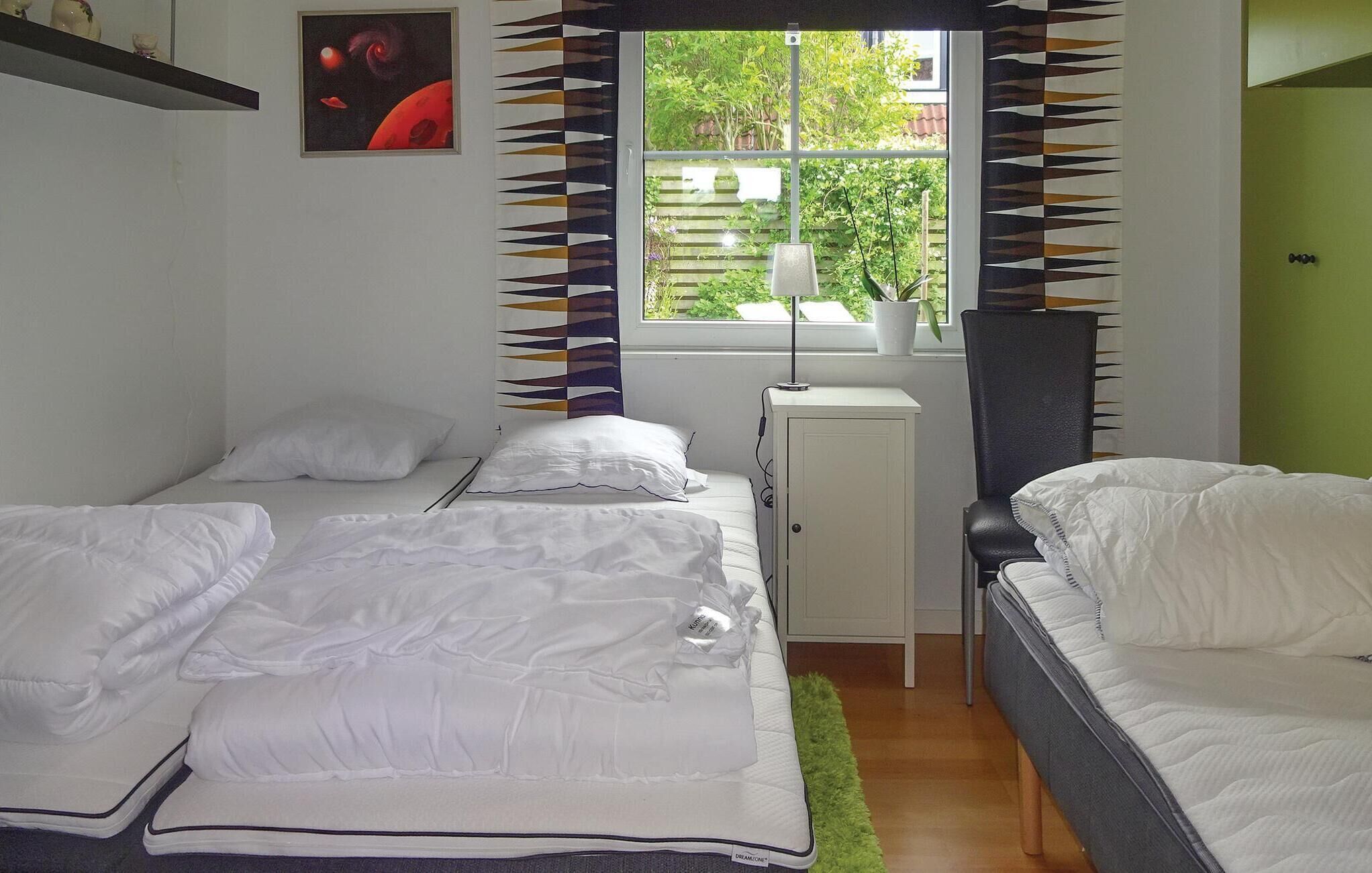 A bedroom with two beds, a window with a view of greenery, a radiator, and a small cabinet.