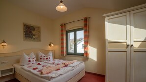 A bedroom with a bed, a wardrobe, a window with curtains, a wall-mounted lamp, and a painting.
