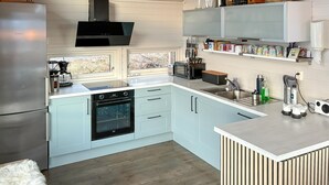 Une cuisine moderne avec des meubles de couleur bleu clair, un réfrigérateur en acier inoxydable, un four encastré et une fenêtre donnant sur un jardin.