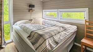 Une chambre à coucher avec un lit, deux fenêtres, une table de chevet et une chaise.