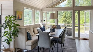Un salon moderne comprenant un canapé, une table à manger, des chaises et une grande fenêtre donnant sur un paysage verdoyant.