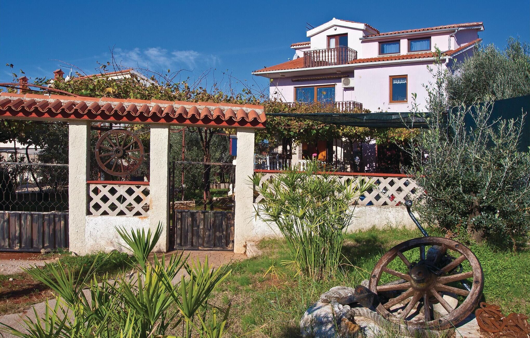 Un edificio tradicional con balcón, un jardín con una noria grande y una valla.