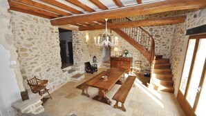 Un intérieur rustique en pierre, avec une table à manger en bois, des bancs et un escalier.