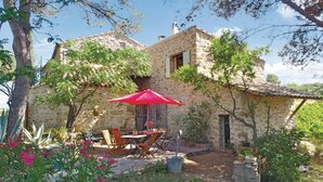 Un bâtiment en pierre doté d’un patio comprenant une table et des chaises, le tout abrité par un parasol rouge.