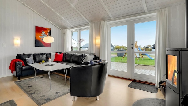 Un salon moderne avec un canapé, une table basse et une cheminée. De grandes fenêtres offrent une vue sur une aire de jeux et un espace extérieur.