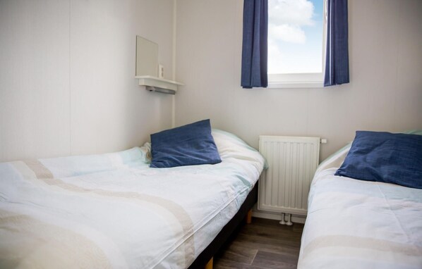 A twin room with two beds, a window with curtains, a radiator, and a small shelf with a mirror.