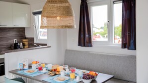 A modern kitchen with a dining table set for breakfast, featuring a wicker pendant light, white cabinets, and a view through the window. - Cozy home in Breukelen with WiFi (Breukelen)