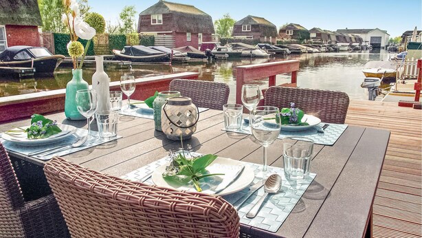 A dining table set with plates, glasses, and cutlery, overlooking a canal with boats and traditional houses. - Cozy home in Breukelen with WiFi (Breukelen)