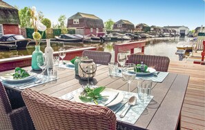 A dining table set with plates, glasses, and cutlery, overlooking a canal with boats and traditional houses.