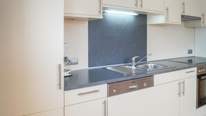 A modern kitchen with white cabinets, a stainless steel sink, and a built-in dishwasher.
