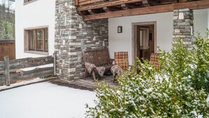 A stone and wood exterior with a porch, two chairs, and a door.