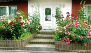 Een huis met een witte voordeur, een bakstenen gevel en een tuin met rozenstruiken.