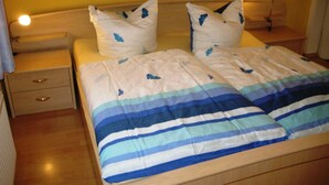 A double bed with a striped bedspread, two pillows with butterfly designs, a wooden nightstand with drawers, and a bedside table with a lamp.