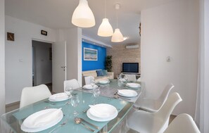 A dining area with a long table set for six, white chairs, and hanging pendant lights.