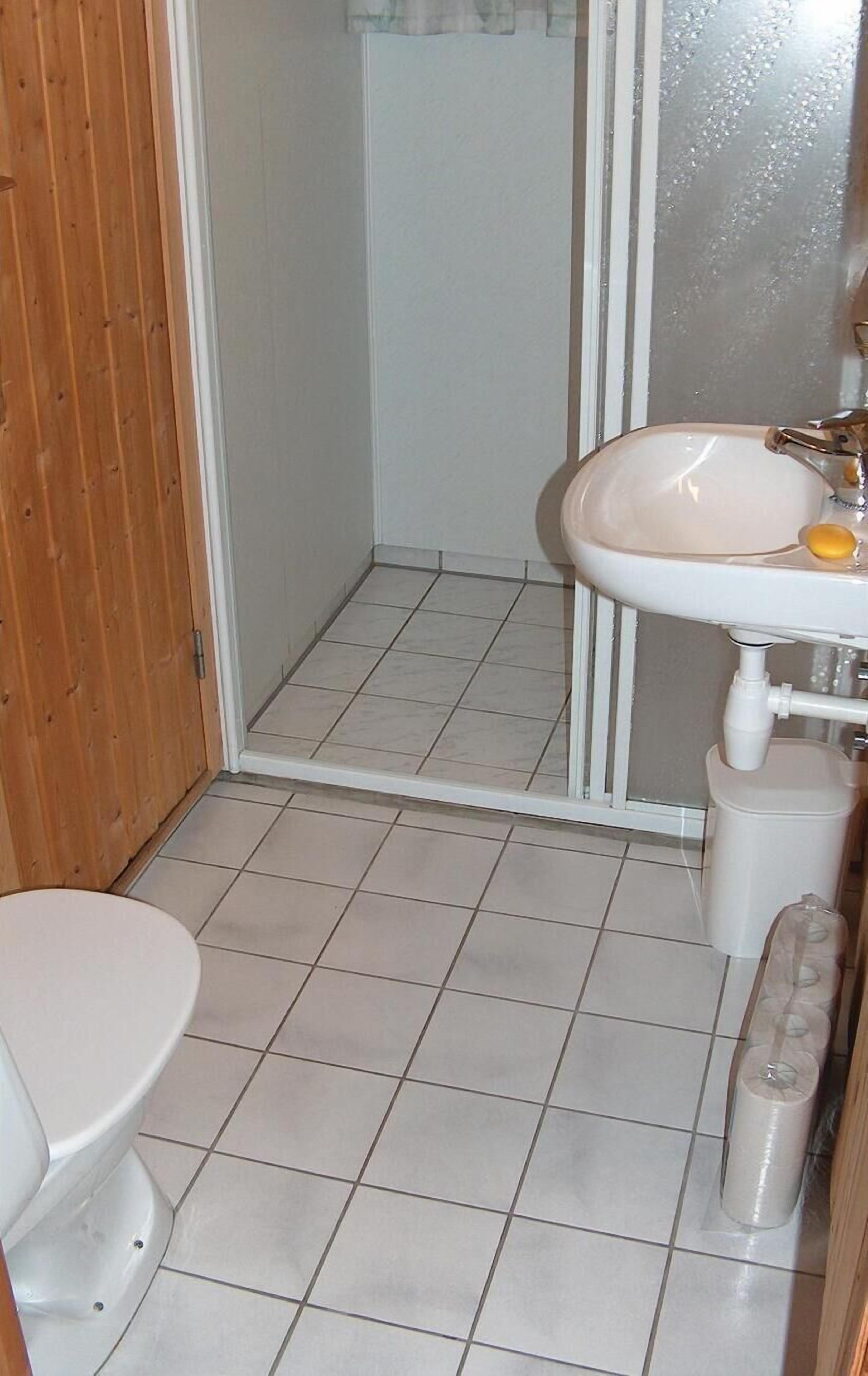 Un baño pequeño con inodoro blanco, lavamanos con espejo y zona de ducha.